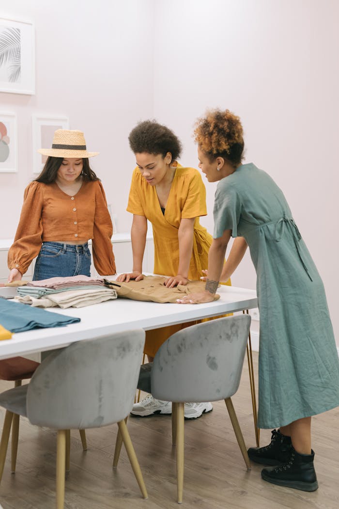 Three women collaborate in a fashion studio, discussing fabrics and designs.
