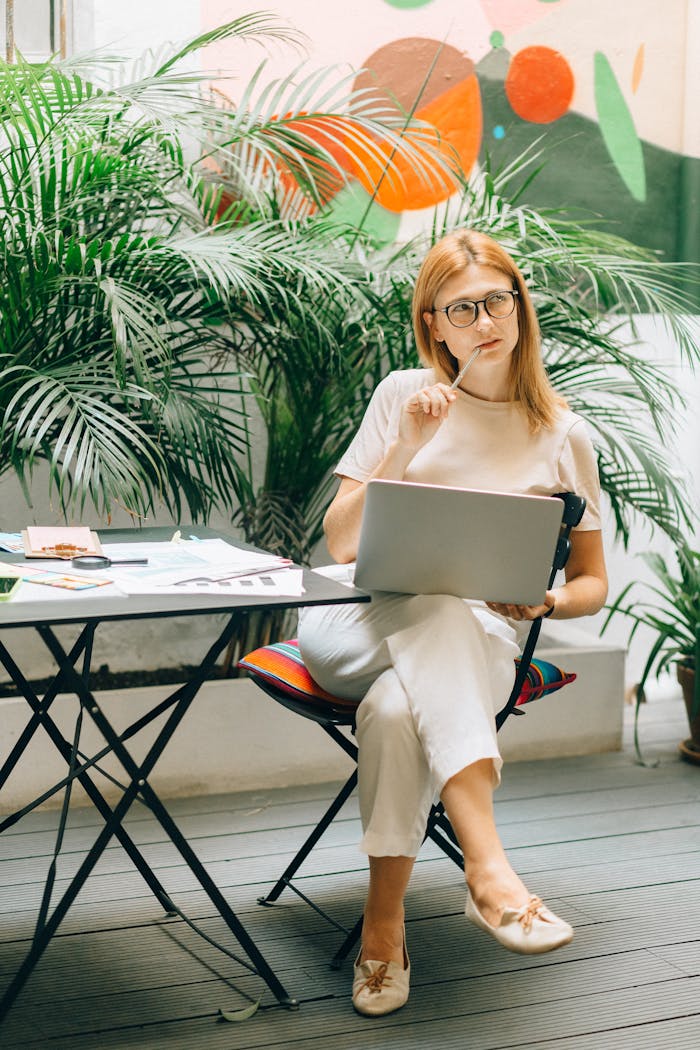 Focused woman in modern workspace with laptop surrounded by greenery, creating a serene work environment.
